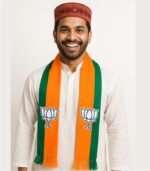 Orange and green BJP scarf with lotus emblem, worn by a smiling man.