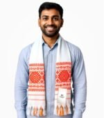 Indian male model wearing traditional Assamese gamcha with orange-red woven border and white base, smiling in a studio setup