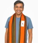 Indian male model wearing orange Madrasi gamcha with green and golden border, smiling in white studio background