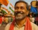 Smiling Bihari man wearing a cotton gamcha during election season with neutral campaign flags in the background